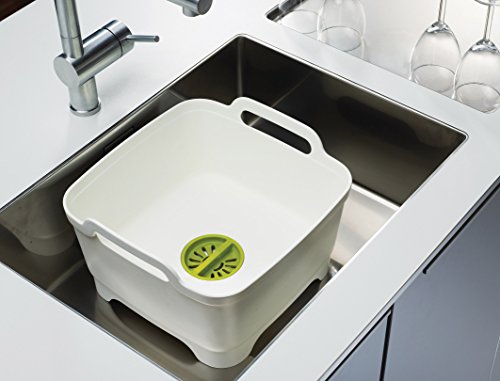 Egouttoir à vaisselle en plastique robuste, blanc et vert, avec système d'évacuation de l'eau de rinçage et poignées latérales. Il se pose dans ou à côté de l'évier. Joseph Joseph